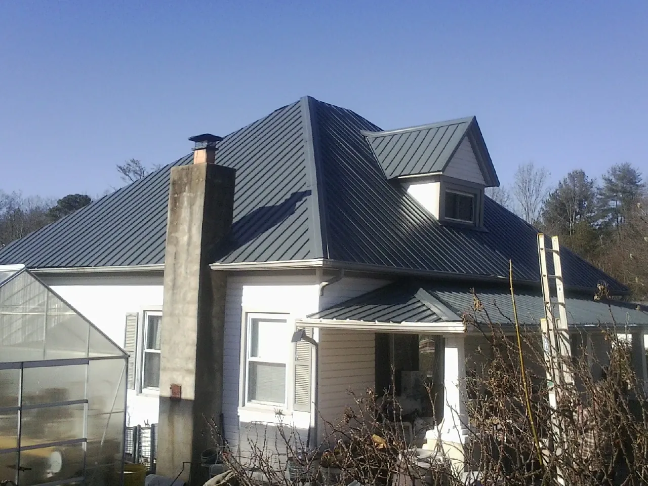 Dark blue standing seam metal roof on a white farmhouse with dormer — Slate & Tile Roof Repair by Roofing Brothers in Montara