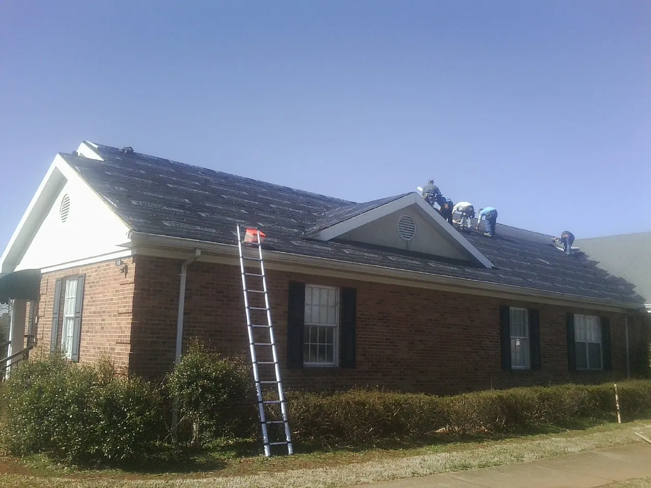 Crew tearing shingles off a brick ranch roof with a ladder set — Metal Roof Repair work by our crew in Montara