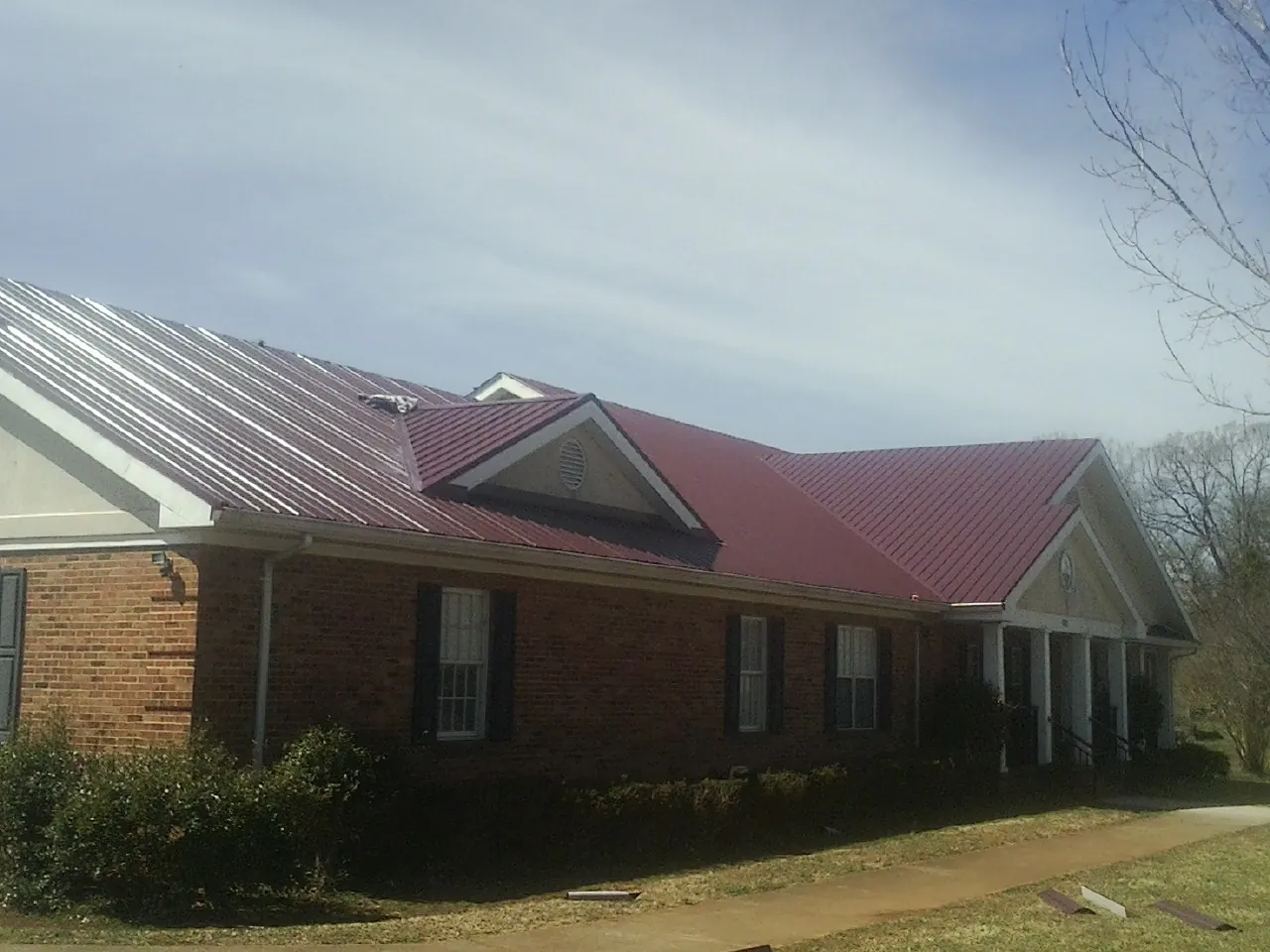 Red metal roof with gabled entries on a long brick building, from a Hail Damage Roof Repair job in Montara
